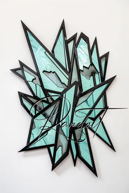 Abstract geometric wall sculpture with black frames and teal glass shards on a white background.