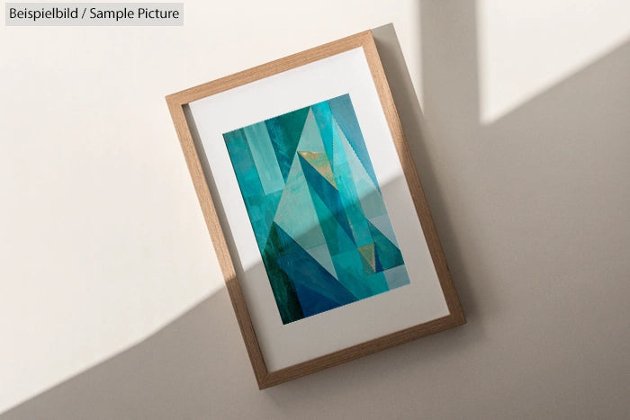 Framed abstract artwork featuring geometric shapes in shades of blue and teal, displayed on a sunlit wall.