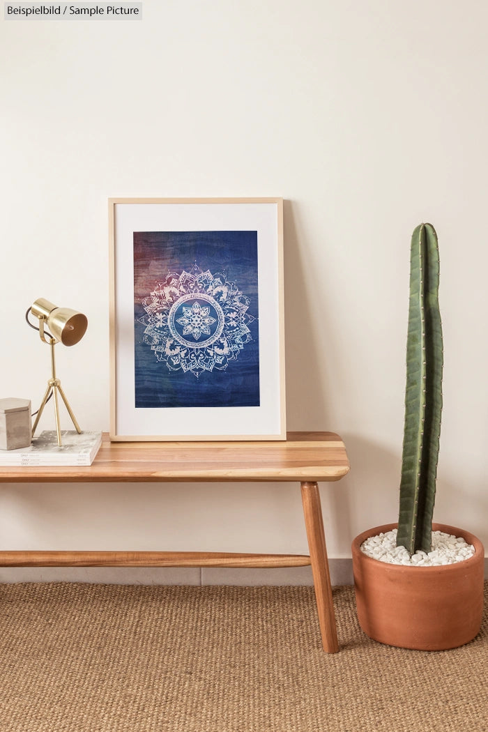 Framed mandala art on wooden bench beside a potted cactus and gold lamp in a minimalistic room.