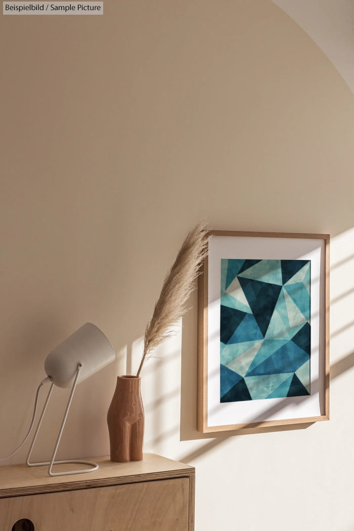 Framed geometric teal art on beige wall, wood shelf with brown vase and white lamp, soft sunlight casting shadows.