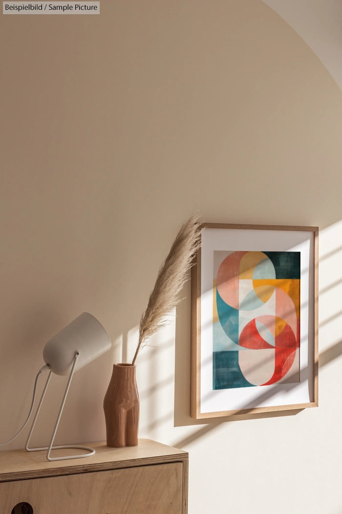 Minimalist interior with abstract art, a brown vase with pampas grass, and a white desk lamp on a wooden surface.