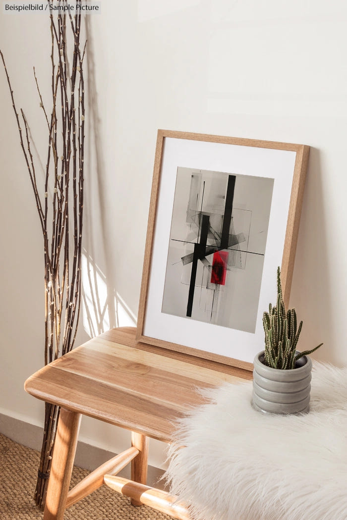 Minimalist room with abstract art, a wooden bench, cactus plant, and decorative branches against a white wall.