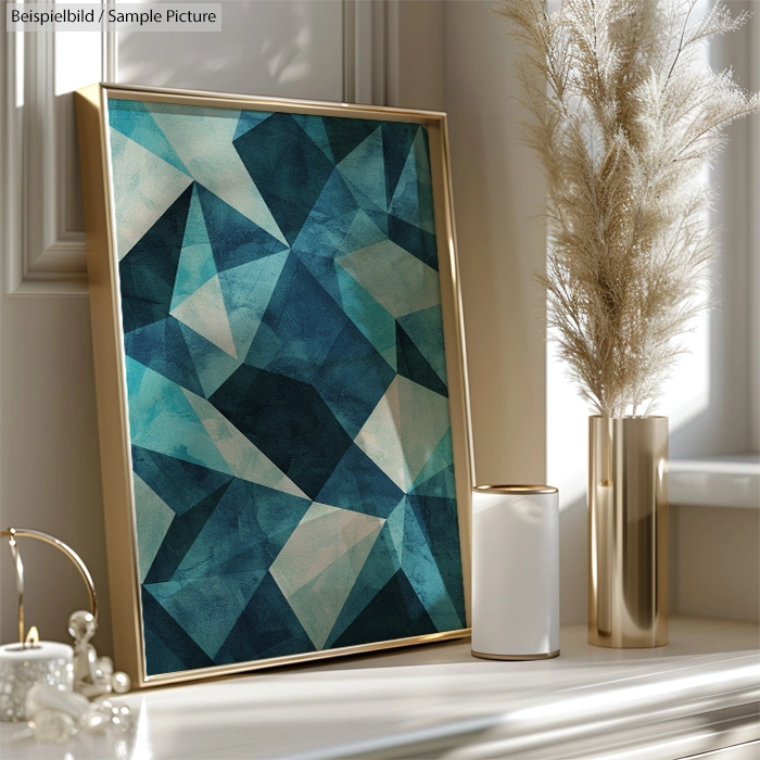 Geometric abstract artwork with blue and teal shades, in a gold frame, next to vases and decorative grass on a windowsill.