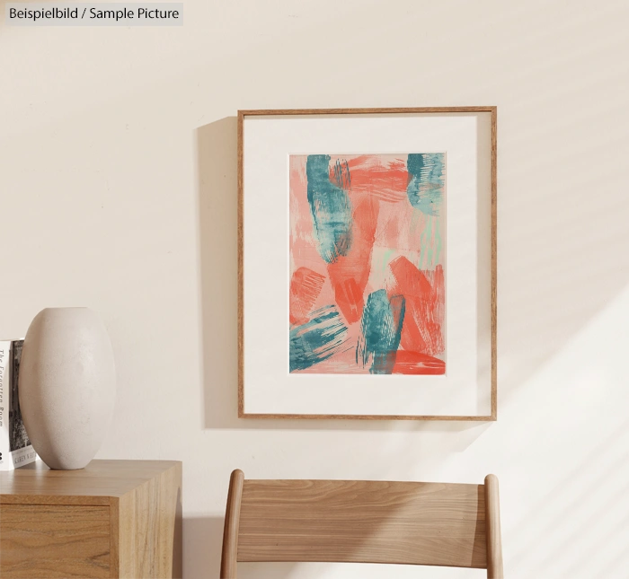 Abstract painting with coral and teal brushstrokes in wooden frame, hung on white wall above wooden table with vase.