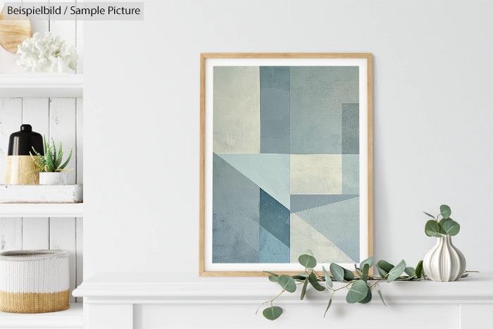 Framed abstract geometric painting in blue and gray tones on a white shelf with decorative plants and baskets.