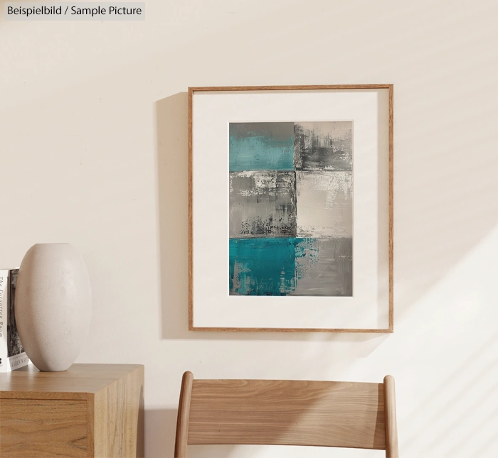 Framed abstract painting with gray and teal geometric patterns hung on a wall above a wooden table.