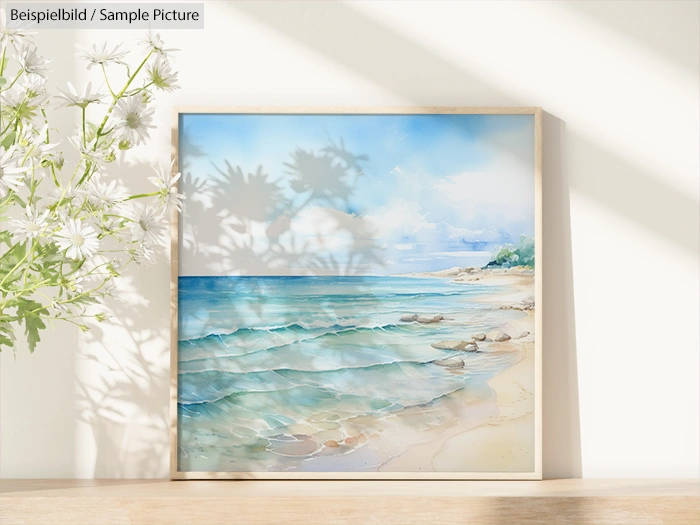 Framed watercolor painting of a serene beach scene with blue skies and soft waves, placed on a sunlit surface.