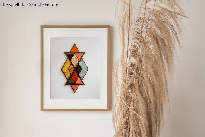 Framed geometric art on a wall next to dried pampas grass, featuring colorful triangles and rhombus shapes.