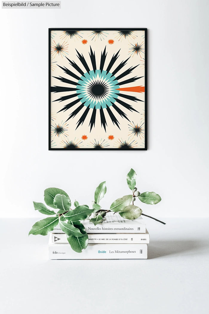 Modern geometric artwork with starburst design in black, teal, and orange, hung above a stack of books and leaves.