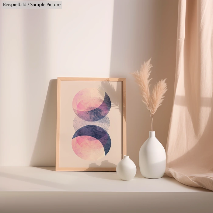 Framed abstract art with pink and purple shapes beside white vases on a sunlit table.