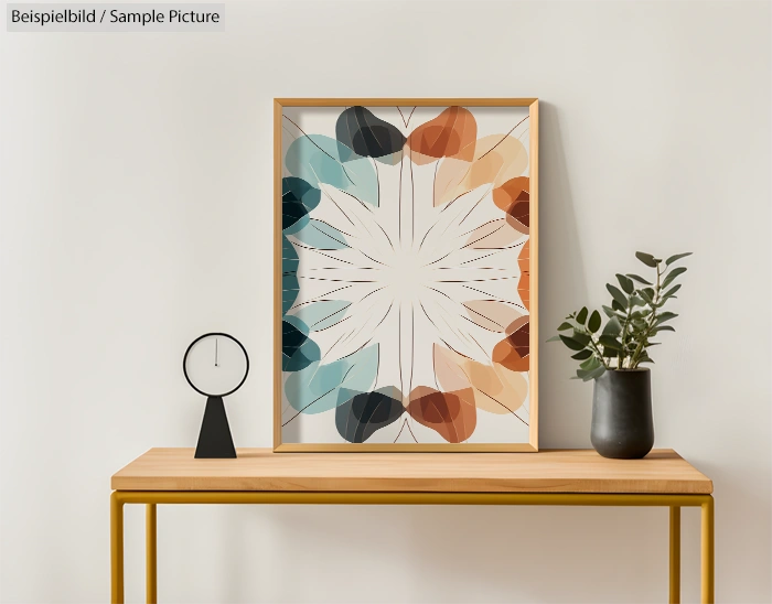 Abstract framed artwork with colorful leaf pattern on a wooden table with a black clock and potted plant.