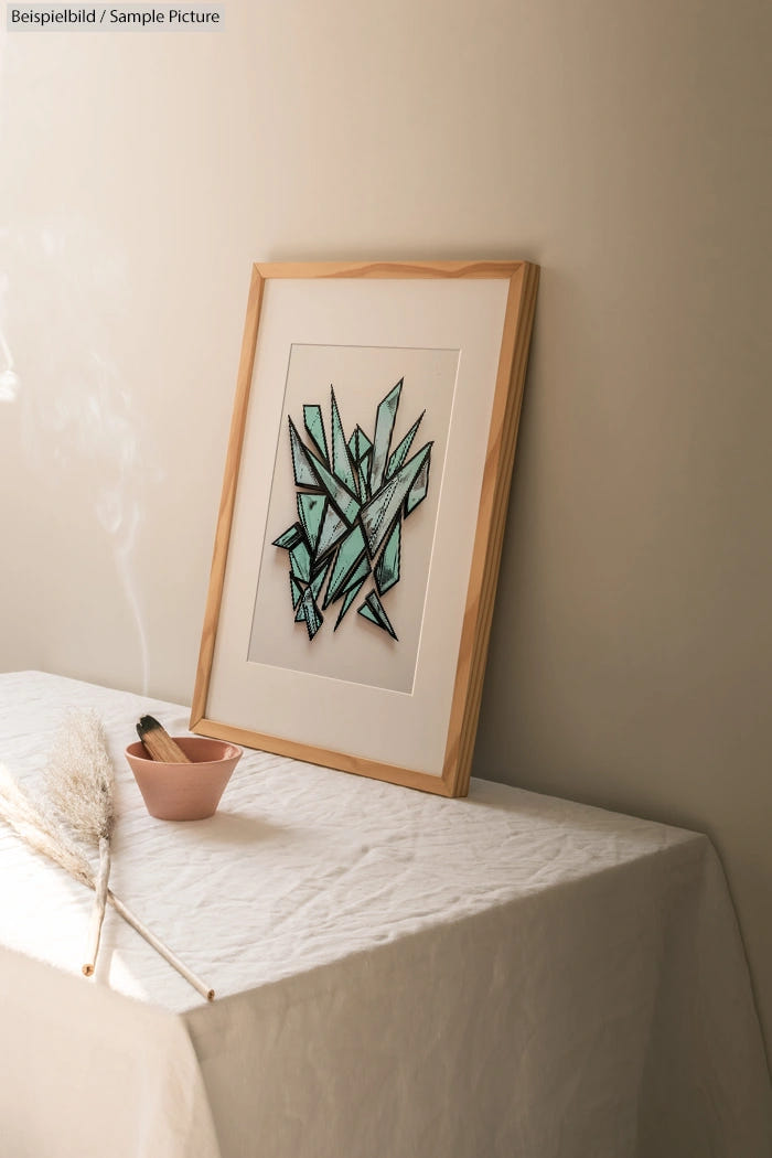 Framed abstract artwork with geometric blue shapes on canvas, placed on a table covered with white cloth.