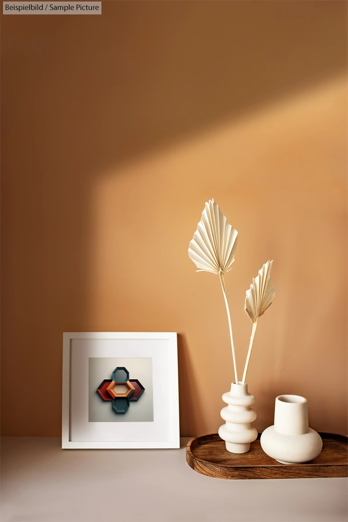 Minimalist decor with framed geometric art, dried palm leaves, and ceramic vases on a wooden tray against a brown wall.