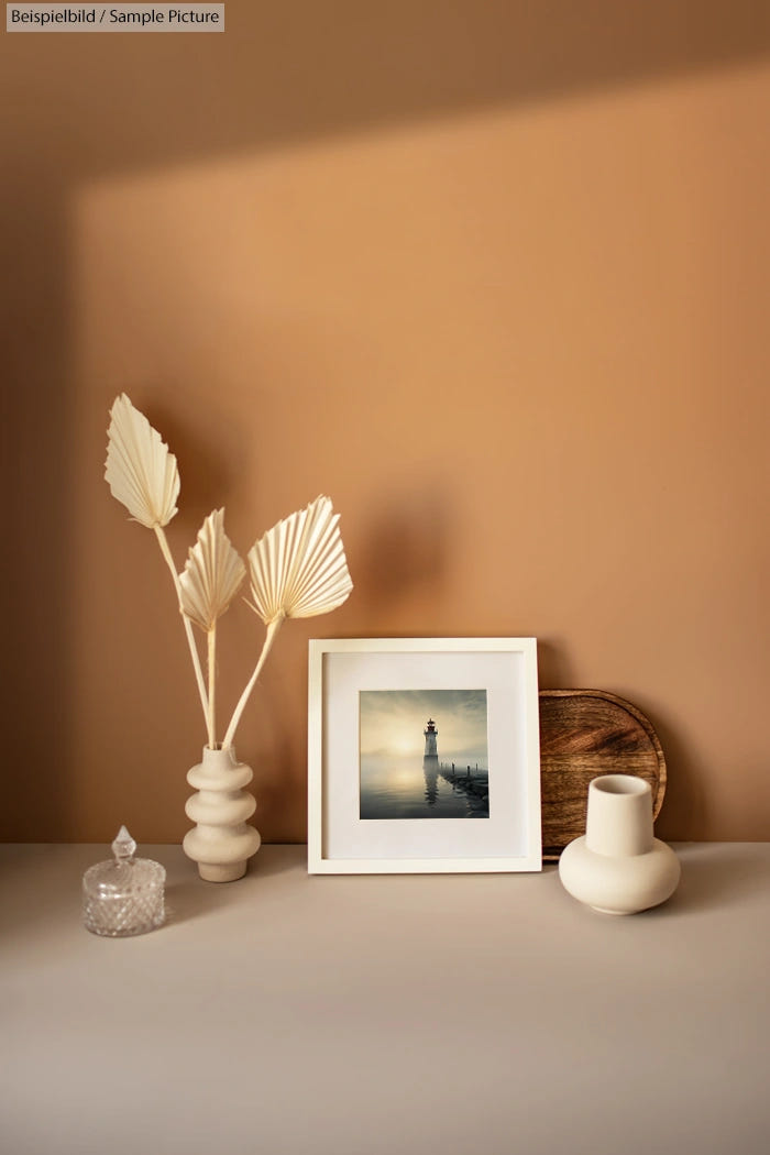 Minimalist beige decor with lighthouse photo, plants in a vase, and ceramic objects on a surface.