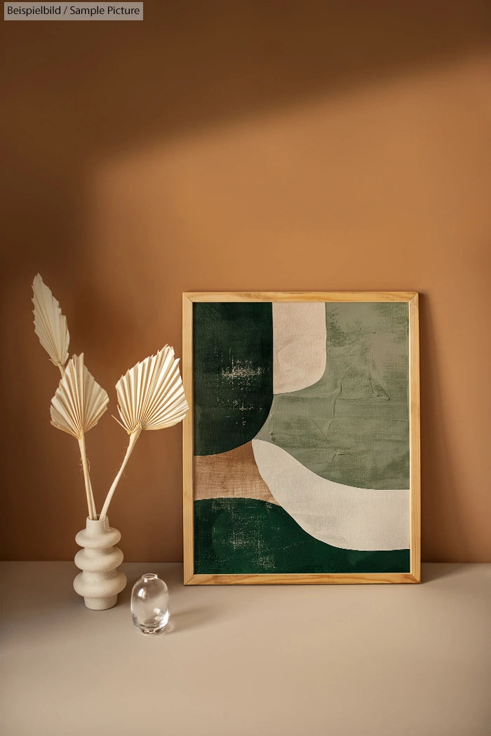 Decorative art print with green, beige abstract shapes in wooden frame, displayed next to modern neutral vase.