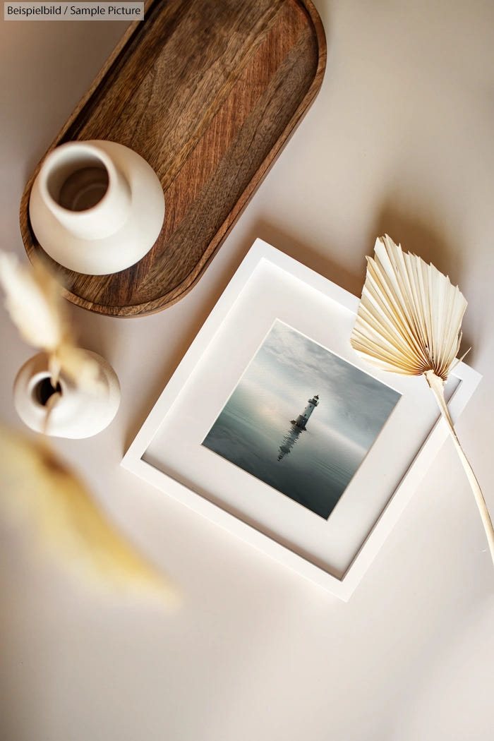 Framed lighthouse photo on table with ceramic vase and dried leaf decor.