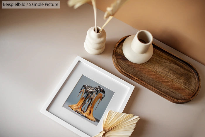 Decorative display with art frame, ceramic vases, tray, and open book on a neutral-toned surface.