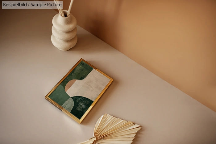 Geometric art in a wooden frame on a beige table beside a decorative vase and a folded magazine.