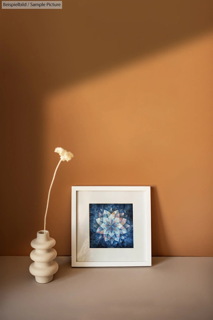 Beige vase with flower beside a framed geometric artwork on a brown shelf with soft lighting.