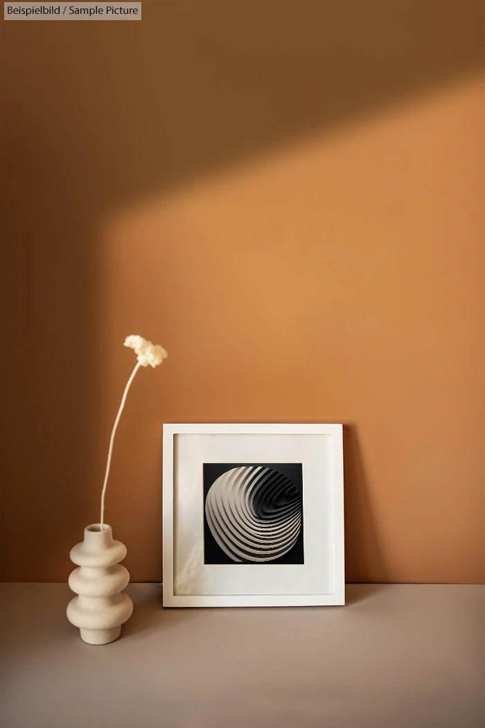 Minimalist beige interior with vase and framed black and white abstract spiral artwork on table under soft lighting.