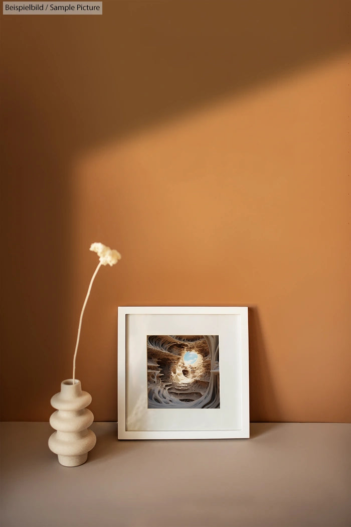 Modern vase with single flower beside framed abstract art on beige surface.