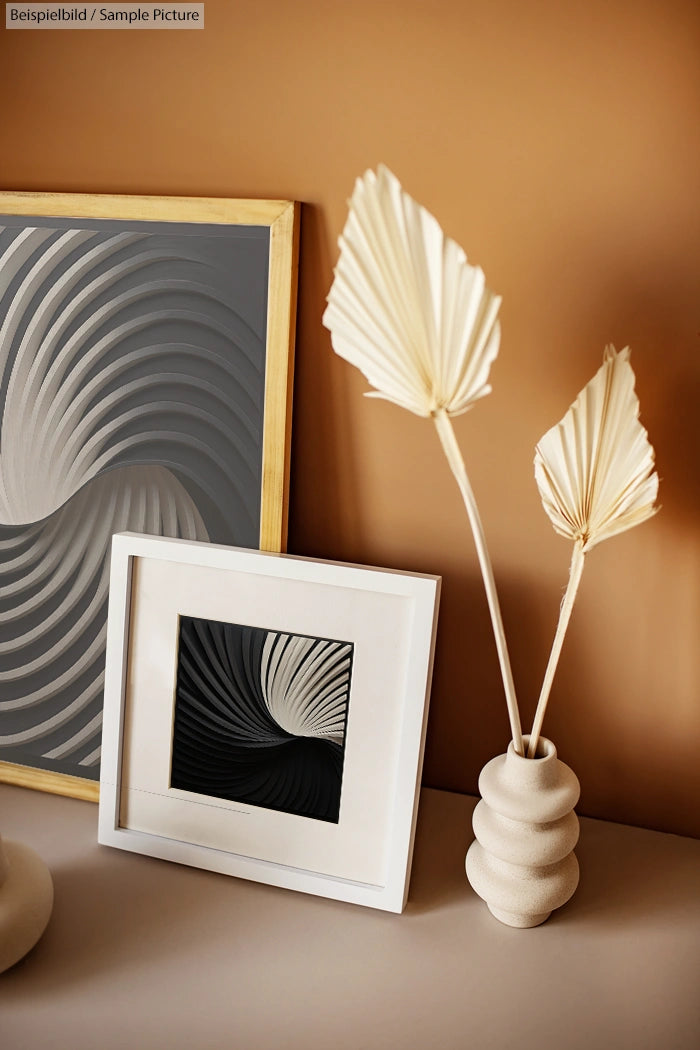 Modern decor with abstract art prints and dried palm leaves in a textured vase on a beige background.