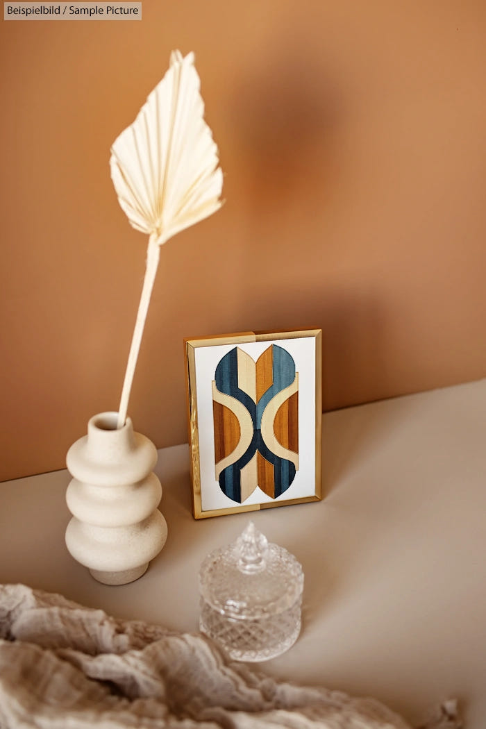 Minimalist decor with a vase, framed abstract art, and a glass jar on a beige tabletop.