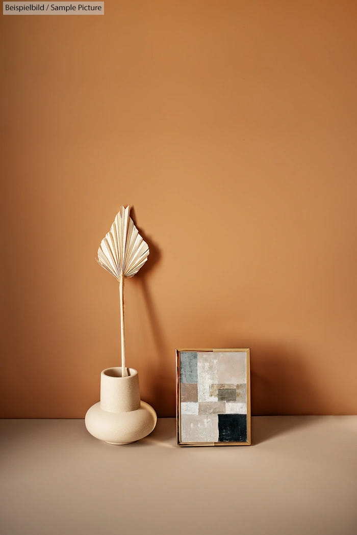 Minimalist decor with dried leaf in vase and abstract painting on beige background.