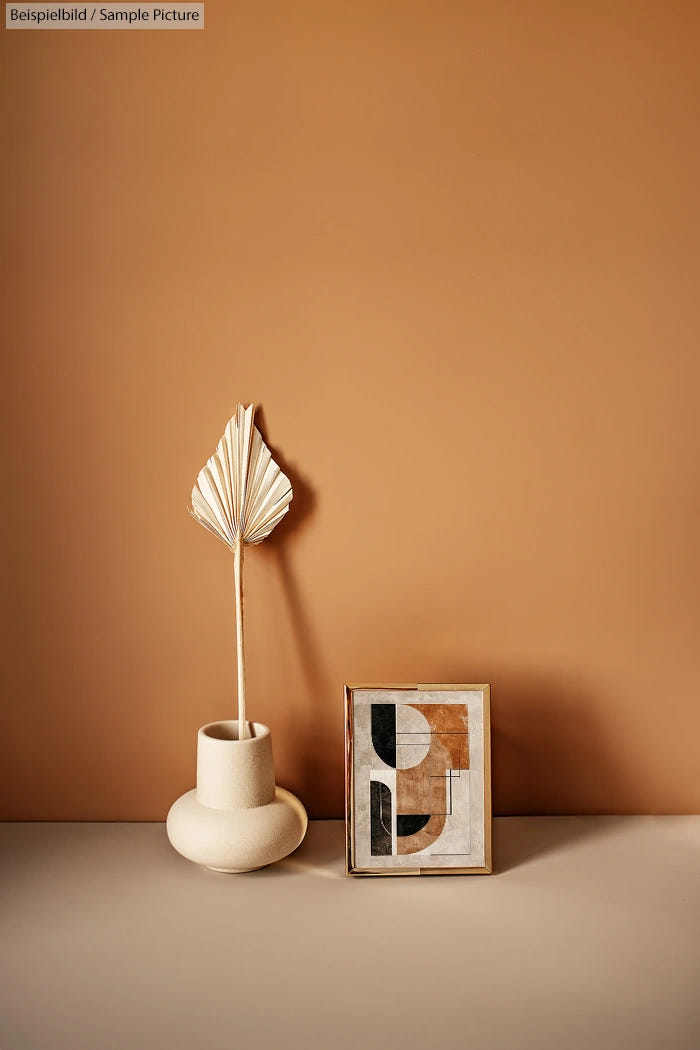 Minimalist decor with a dried leaf in a vase and abstract art on a beige background.