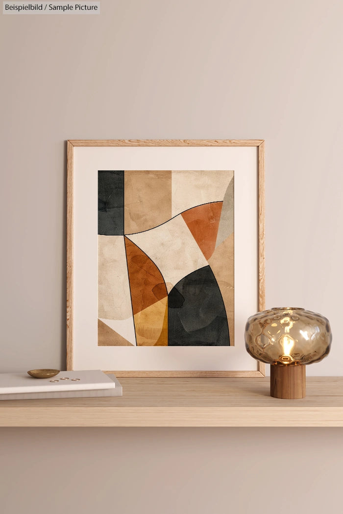 Abstract geometric art in natural tones, framed on a light wood shelf with a decorative glass lamp and closed book.