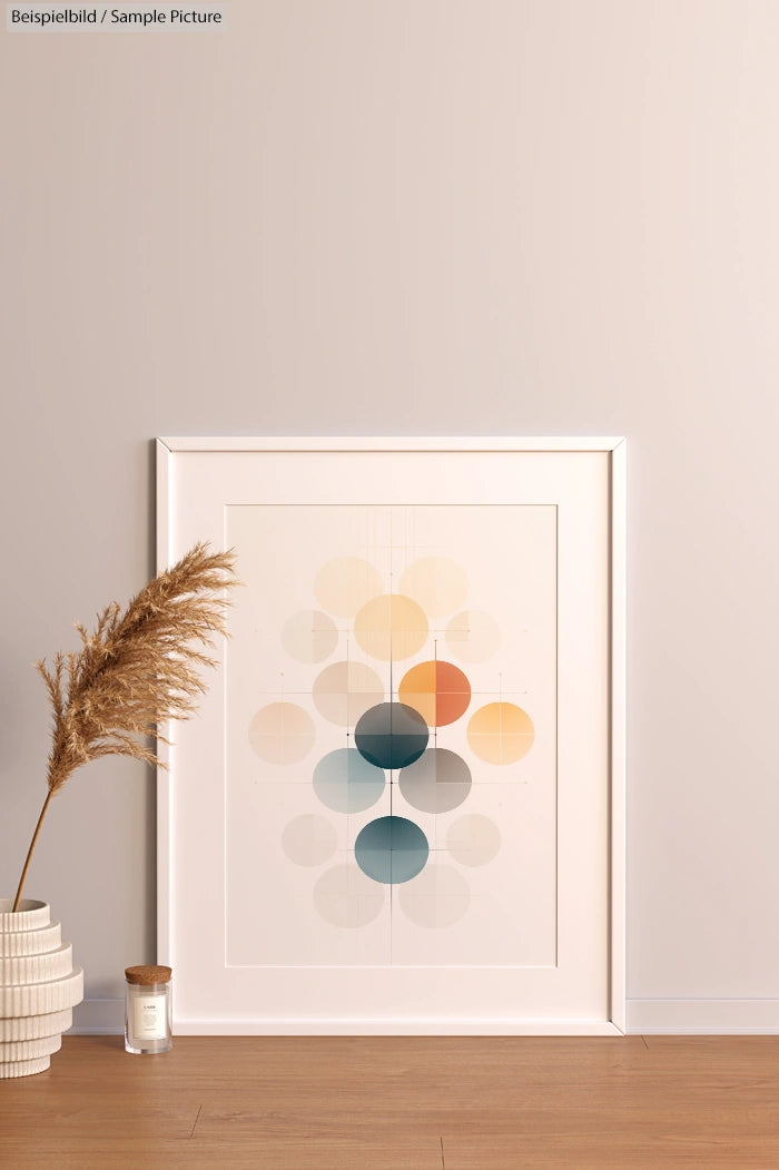 Minimalist framed geometric art print with circular patterns in earthy tones, placed on wooden floor with pampas grass decor.