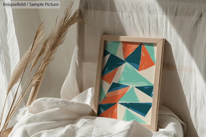 Framed abstract geometric art with orange, teal, and beige triangles on white draped fabric background.