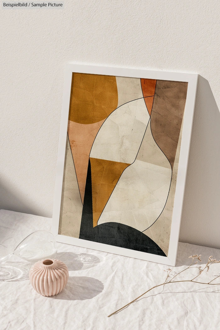 Framed geometric abstract art print on a white surface with a decorative vase and dried flowers.