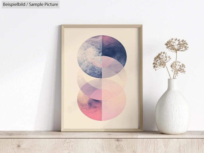 Framed abstract print with pastel pink and navy overlapping circles, next to a vase with dried flowers on a wooden shelf.