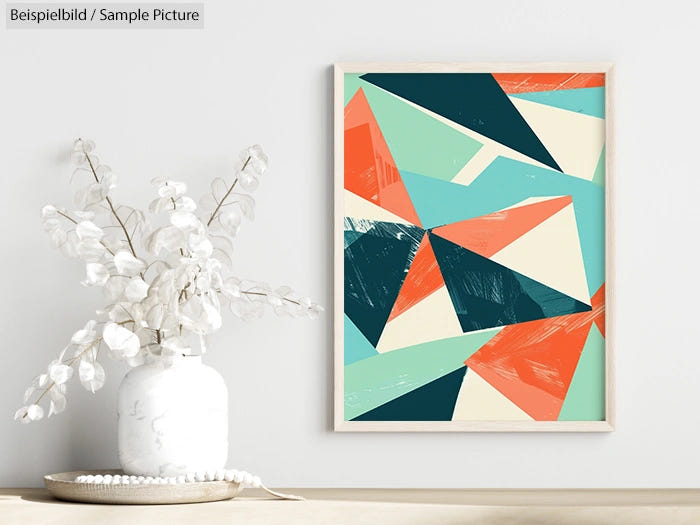 Modern abstract art with geometric shapes in teal, coral, and beige on a wall above a vase with white branches.