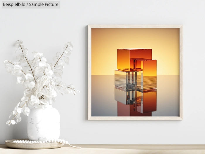 Framed abstract art with amber glass cubes on a reflective surface, set on a wall above a minimalist white vase.