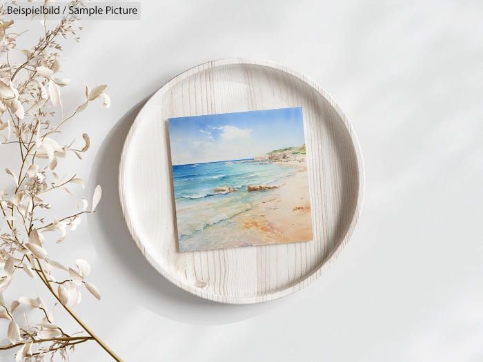 Beach painting displayed on a round wooden board with dried flowers beside it.