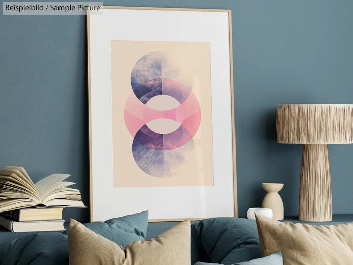 Framed abstract art with overlapping circles in blue and pink, on a blue wall with a lamp and books on a table.