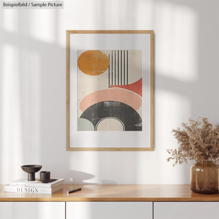 Framed abstract art with geometric shapes on a white wall, wooden console below with decor items and dried flowers.