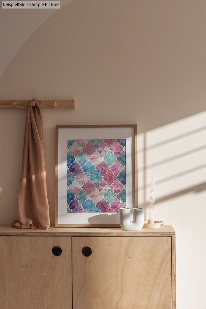 Modern wooden cabinet with framed geometric art, a beige drape, and a white vase in a sunlit room.