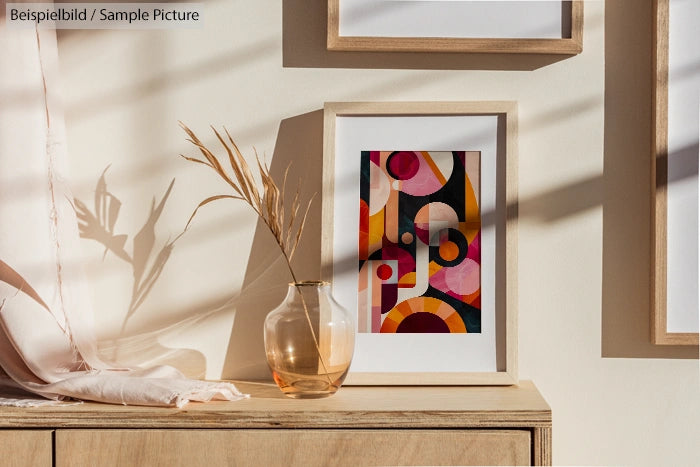 Abstract geometric art in wooden frame on a table with dried plants in glass vase.