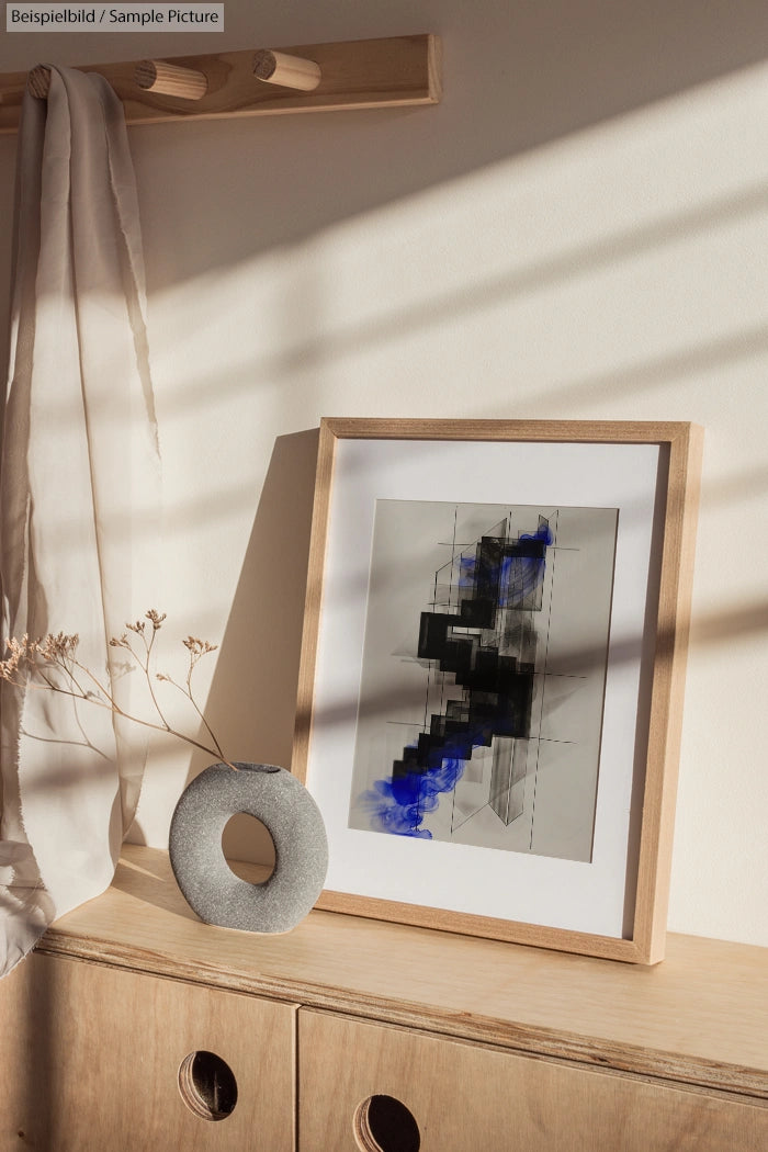 Modern abstract art in frame with blue and black design on a wooden cabinet, next to circular stone decor and white curtain.