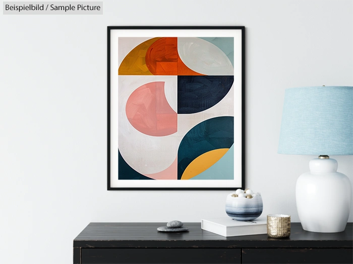 Abstract geometric art with colorful shapes, framed and hanging above a black table with decor and a blue lamp.