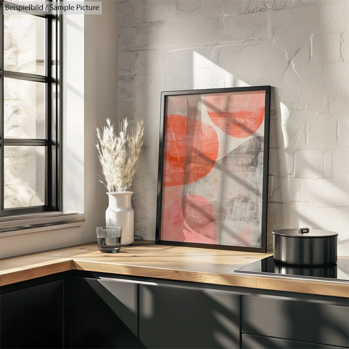 Modern kitchen with minimalist decor, featuring a framed abstract art piece and a vase with dried plants.