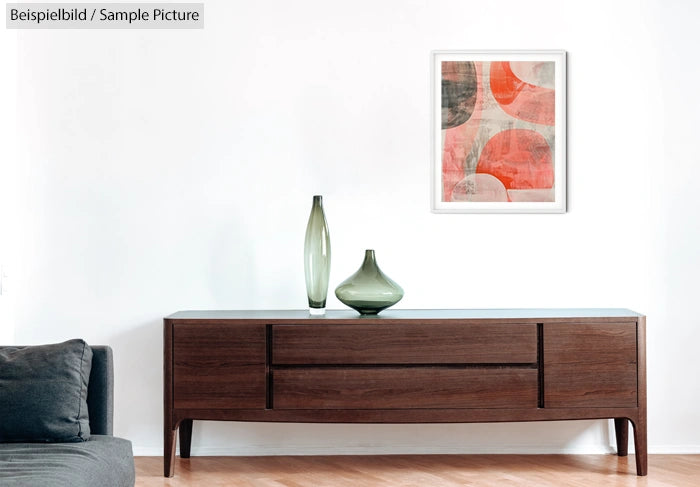 Modern living room with wooden sideboard, green vases, abstract framed art, and gray sofa against a white wall.