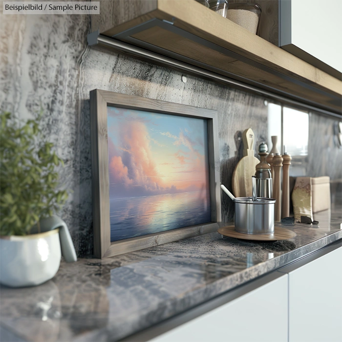 Modern kitchen counter with a framed sunset painting, green plant, and cooking utensils on a marble surface.