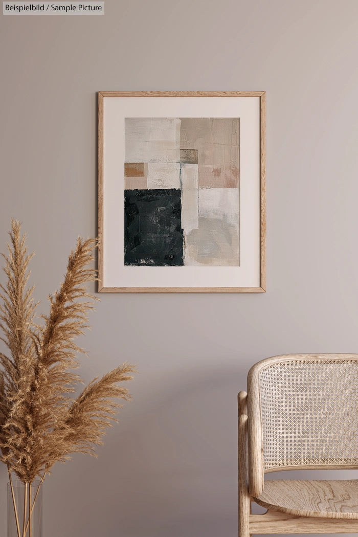 Minimalist abstract art in a wooden frame on a neutral wall, next to a beige wicker chair and pampas grass decor.