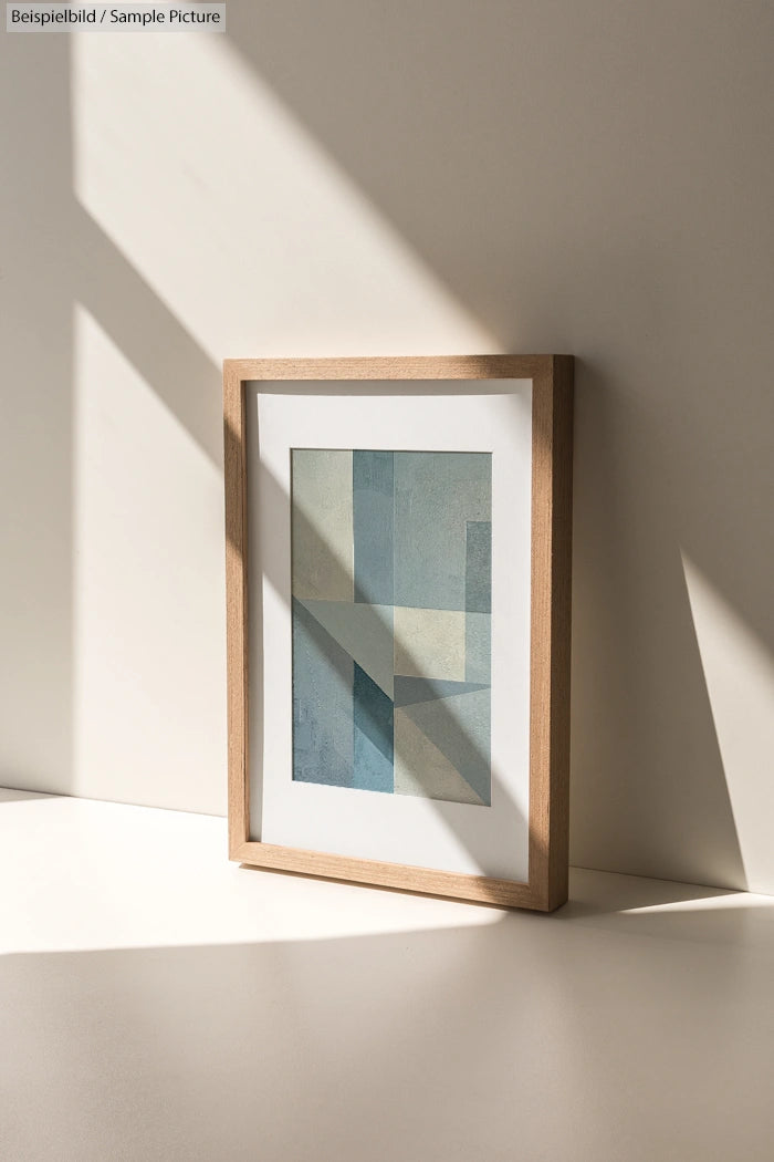 Framed abstract painting with geometric shapes, displayed on a sunlit beige wall.