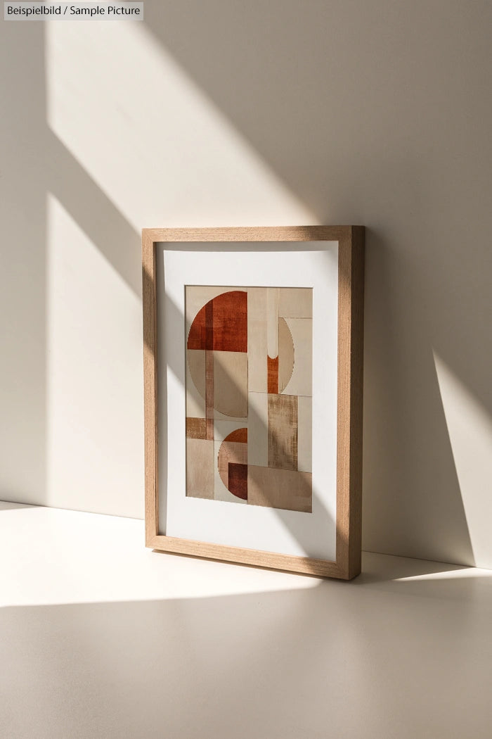 Framed abstract geometric artwork in neutral tones with shadows on a white surface.