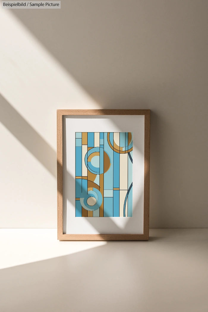 Framed abstract art with geometric shapes in blue, orange, and beige tones, displayed against a sunlit wall.